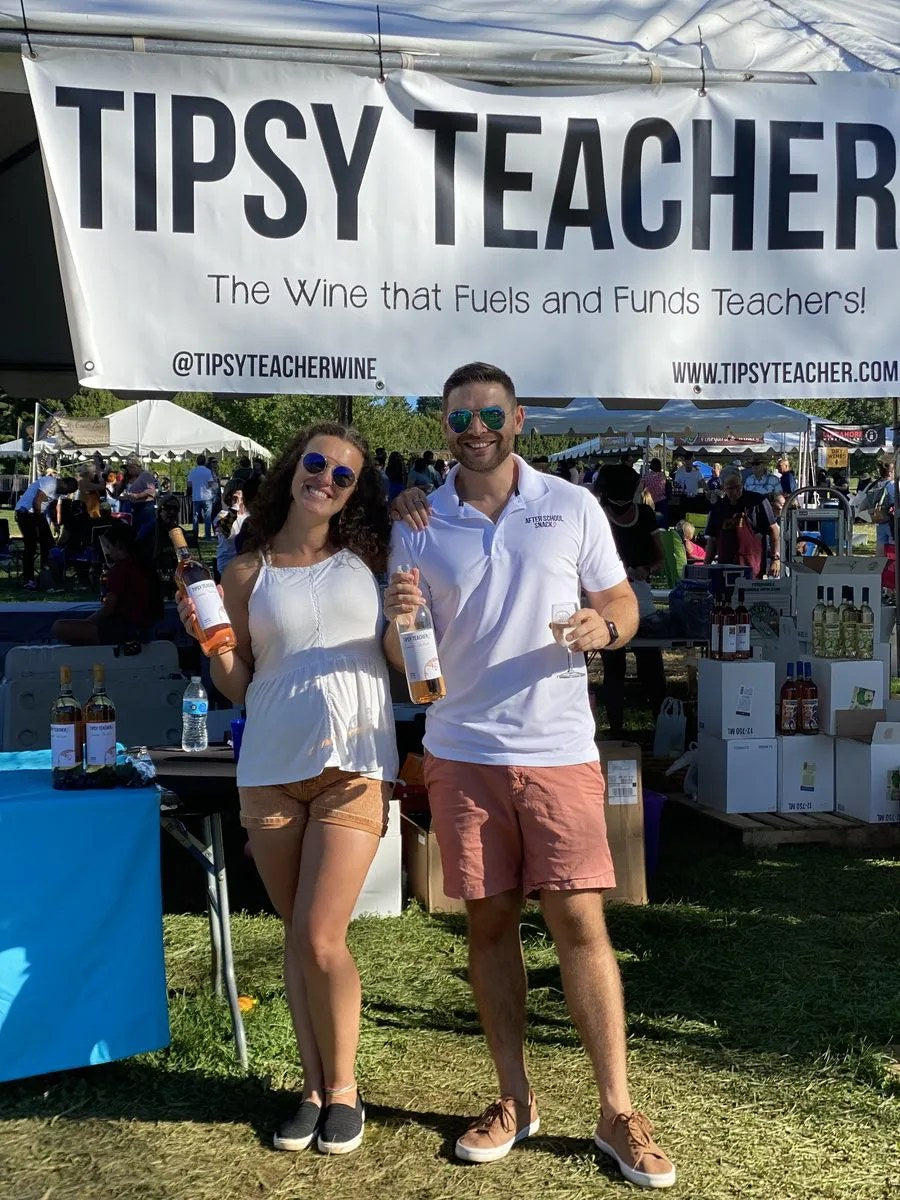 Kenny and Britt pouring at a wine festival in front of the Tipsy Teacher banner